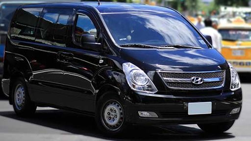 A eight-passenger rental car, a Hyundai Starex, is driving on the road